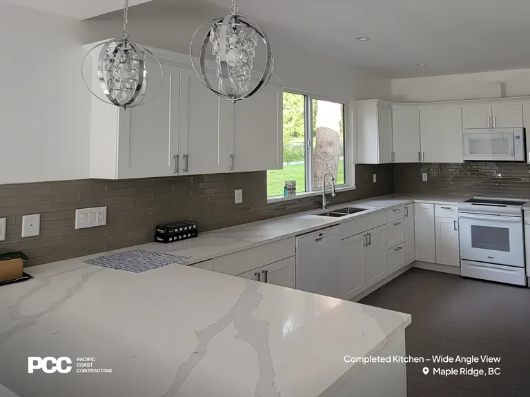 A wide-angle view of a completed modern kitchen remodel by Pacific Coast Contracting in Maple Ridge, BC. The space features custom white cabinetry, a grey subway tile backsplash, white quartz countertops with grey veining, and decorative spherical crystal pendant lights by PCC - Pacific Coast Contracting.