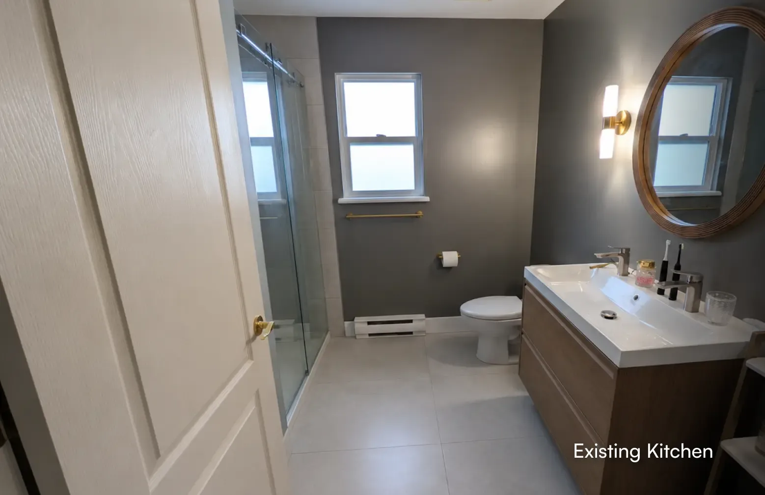 A completed bathroom renovation featuring a modern wooden double vanity, dark grey walls, and a glass-enclosed shower by PCC Renovations.