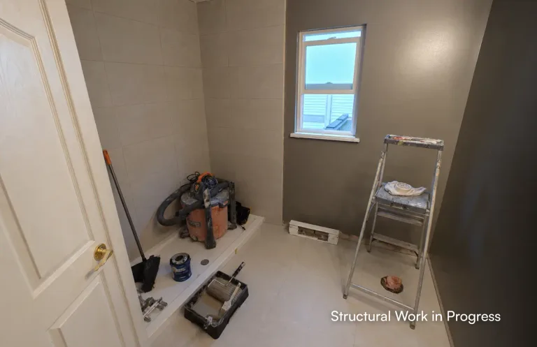 A bathroom under construction showing a newly installed white shower base, large wall tiles, a wet/dry vacuum, and a stepladder by PCC - Pacific Coast Contracting Vancouver.