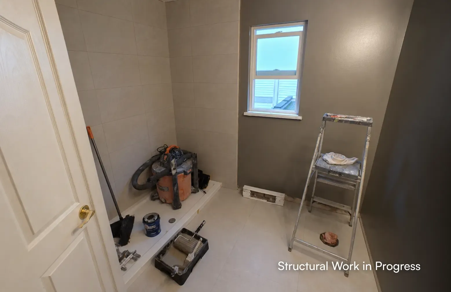 A bathroom under construction showing a newly installed white shower base, large wall tiles, a wet/dry vacuum, and a stepladder by PCC - Pacific Coast Contracting Vancouver.