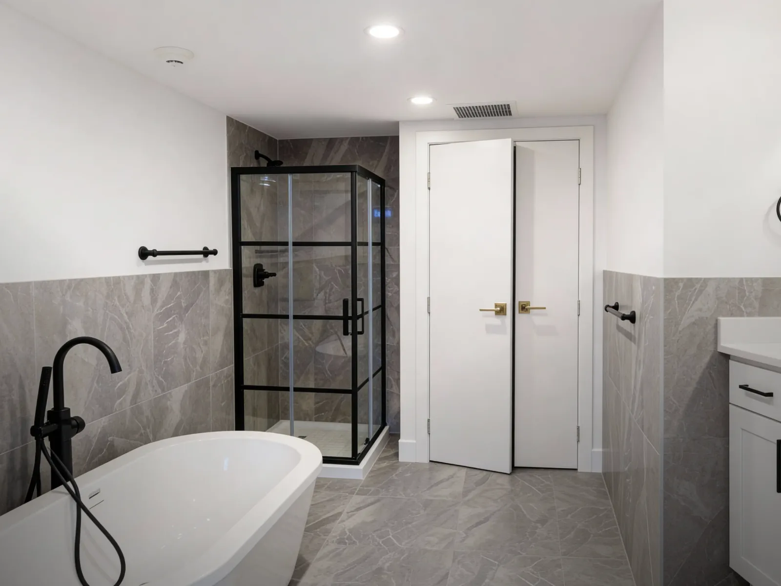 Renovated bathroom with a freestanding white tub, black floor-mounted faucet, framed glass shower and grey stone-look tile in a renovated Langley, BC condo by PCC Renovations.