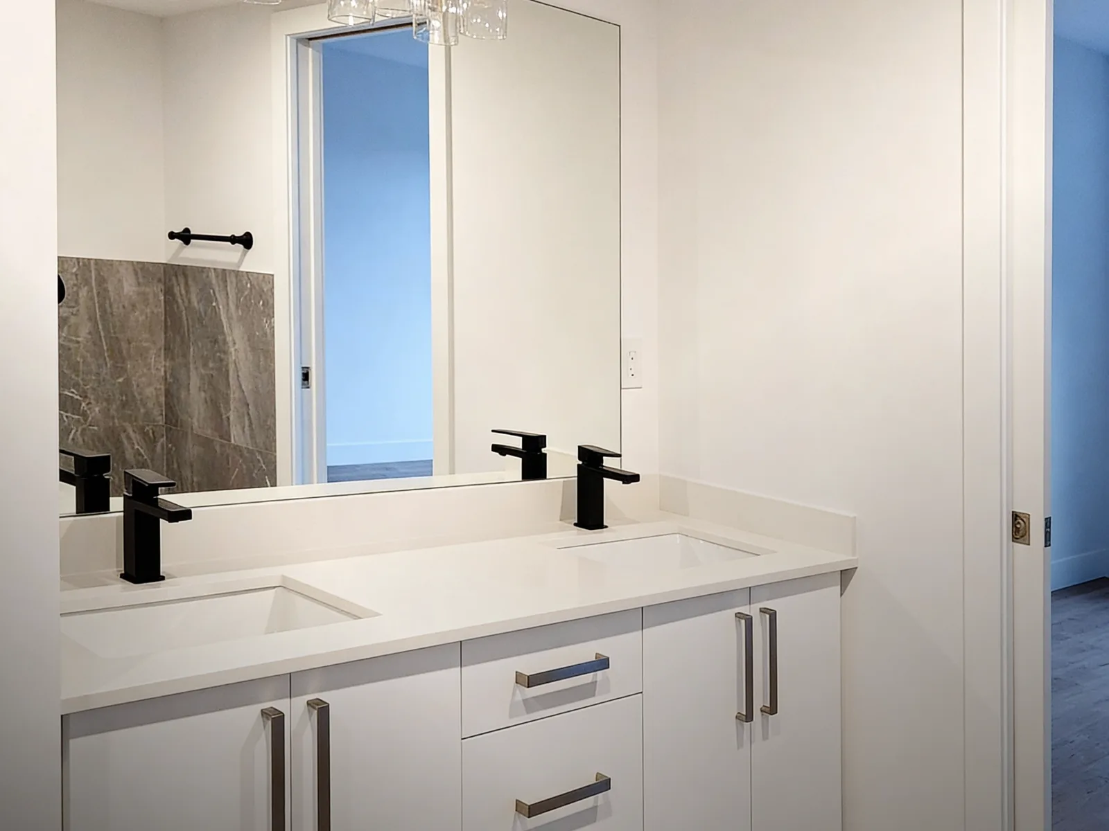 Bathroom with a white double vanity, quartz countertop, black faucets and a large mirror in a renovated Langley, BC condo by PCC Renovations.