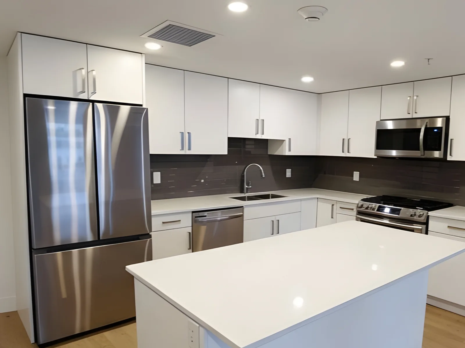Renovated open kitchen with white cabinets, a stainless steel French-door refrigerator, a gas range and a white quartz island in a renovated Langley, BC condo by PCC Renovations.