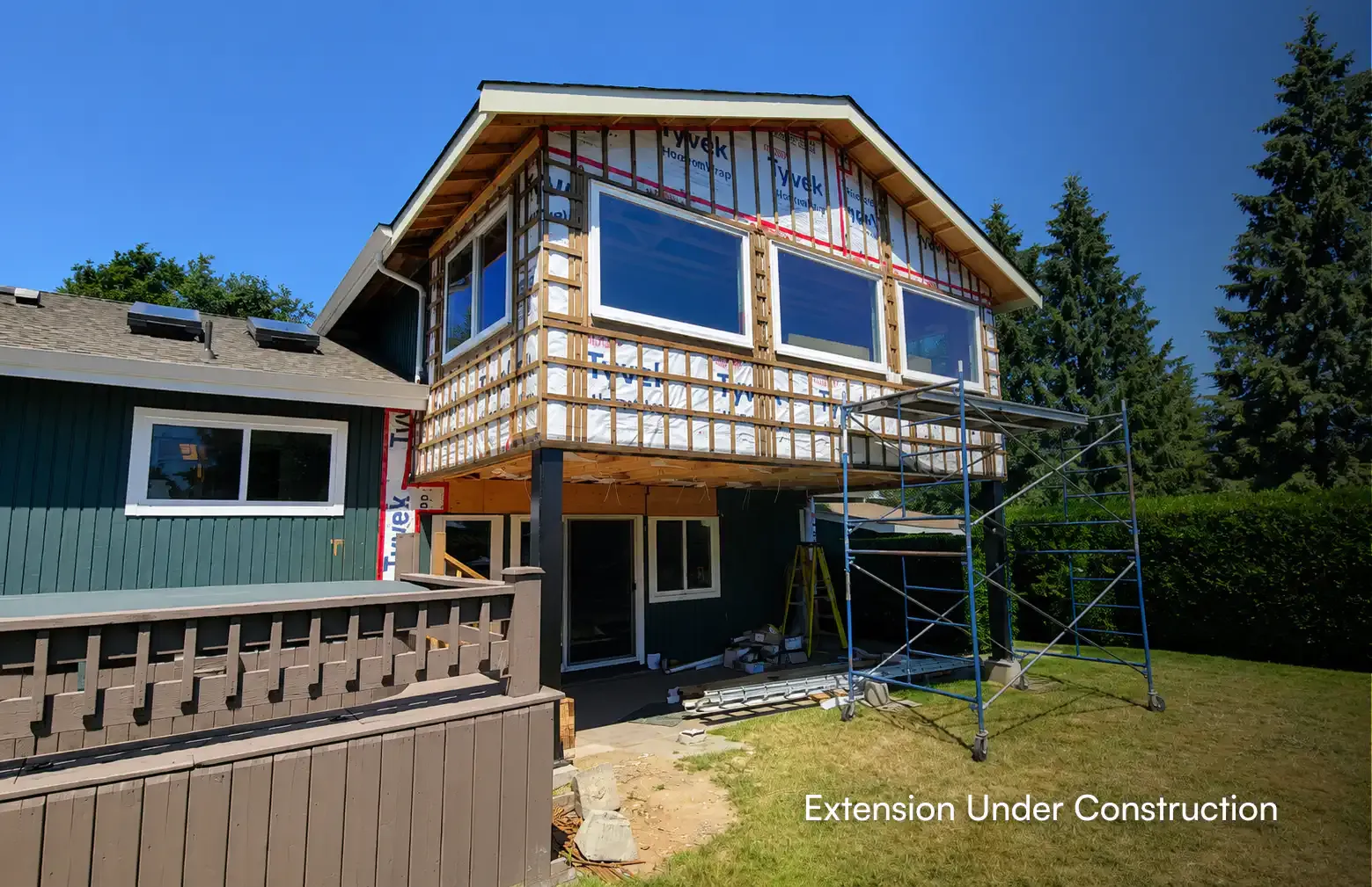 Home extension project under construction in Coquitlam, displaying structural wood framing, Tyvek weather wrap, recently installed windows, and exterior scaffolding by Pacific Coast Contracting.