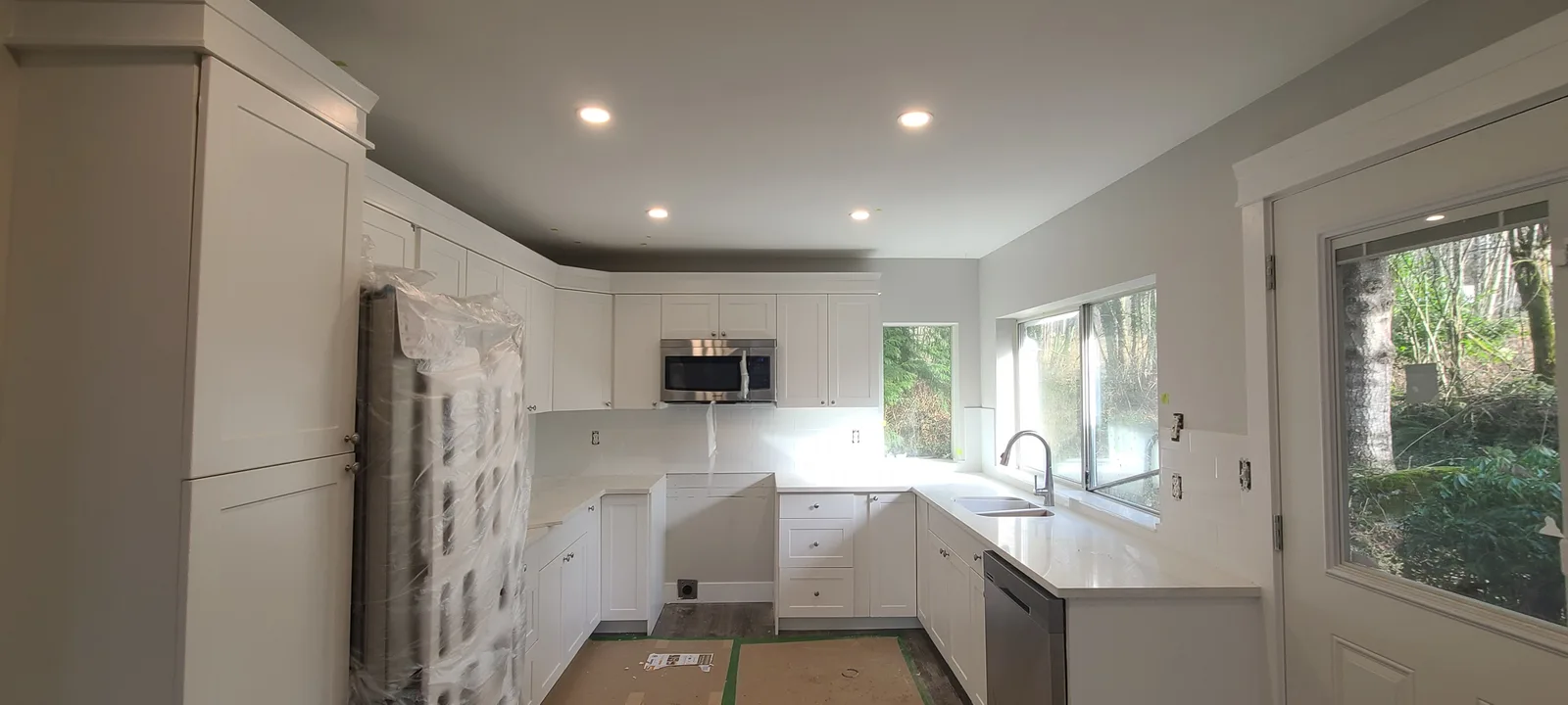 Renovated white kitchen with shaker cabinets, a stainless steel microwave and dishwasher, quartz countertops and recessed lighting in a Maple Ridge, BC house flip by PCC Renovations.