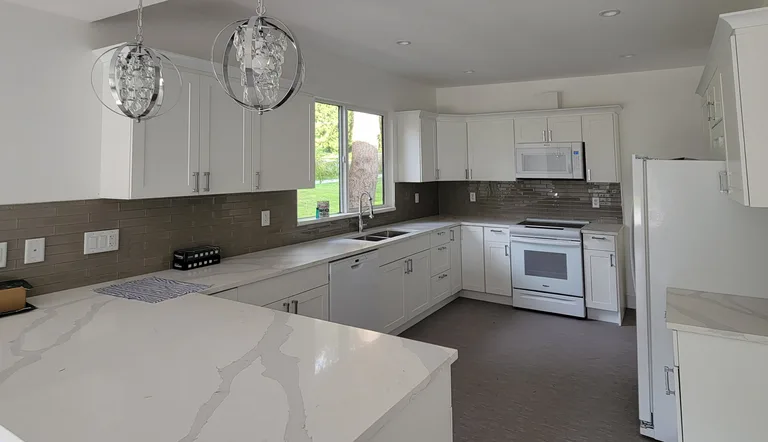 New white kitchen with quartz countertops, glass tile backsplash and pendant lights after an interior renovation in Maple Ridge, BC by PCC Renovations.