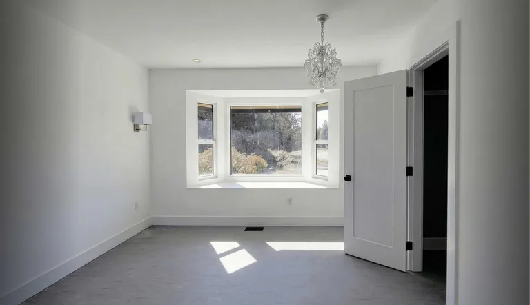 Finished bright bedroom with a white bay window, crystal chandelier and new flooring after an interior renovation in Maple Ridge, BC by PCC Renovations.