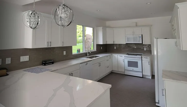 New white kitchen with quartz countertops, glass tile backsplash and pendant lights after an interior renovation in Maple Ridge, BC by PCC Renovations.