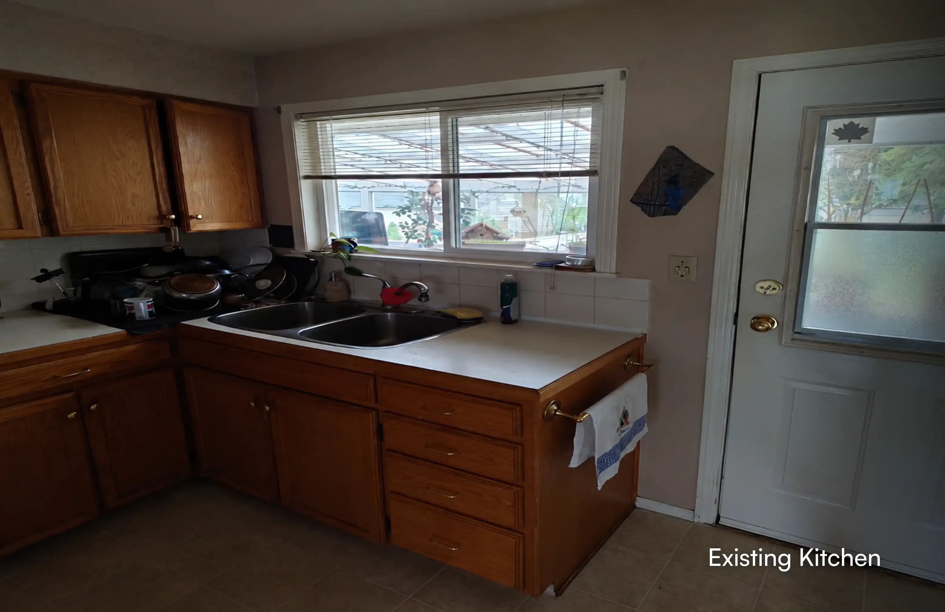 Overview of an existing kitchen with classic wooden cabinetry and window before a custom home renovation by PCC Renovations in Maple Ridge.