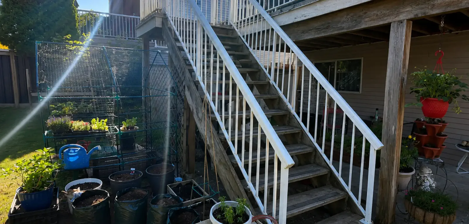 Wide exterior shot of aging wooden deck steps surrounded by potted garden plants in Maple Ridge, prior to structural repair services provided by PCC Decking.