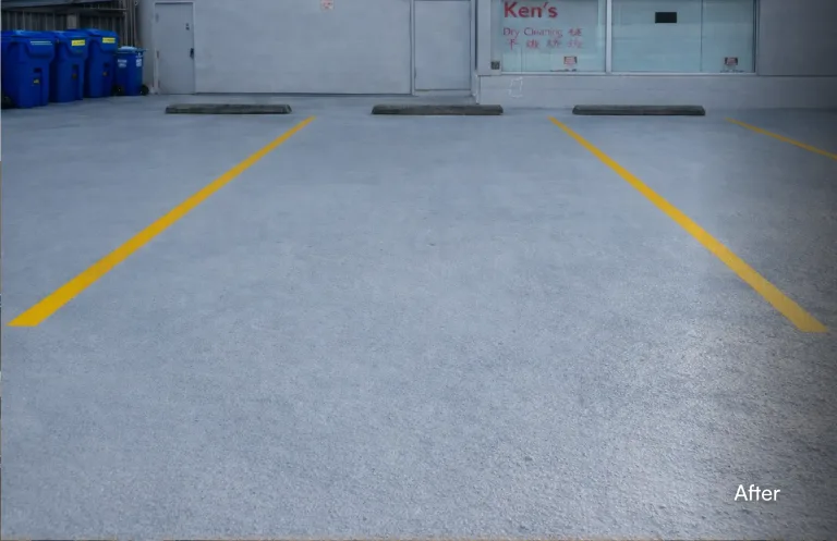 An older, worn commercial parking lot before resurfacing. The concrete is stained, uneven, and faded, with barely visible remnants of old yellow parking lines. A metal storm drain grate is visible on the right. The building in the background has a "Ken's Dry Cleaning" sign. The word "Before" is overlaid in the bottom right corner. — after