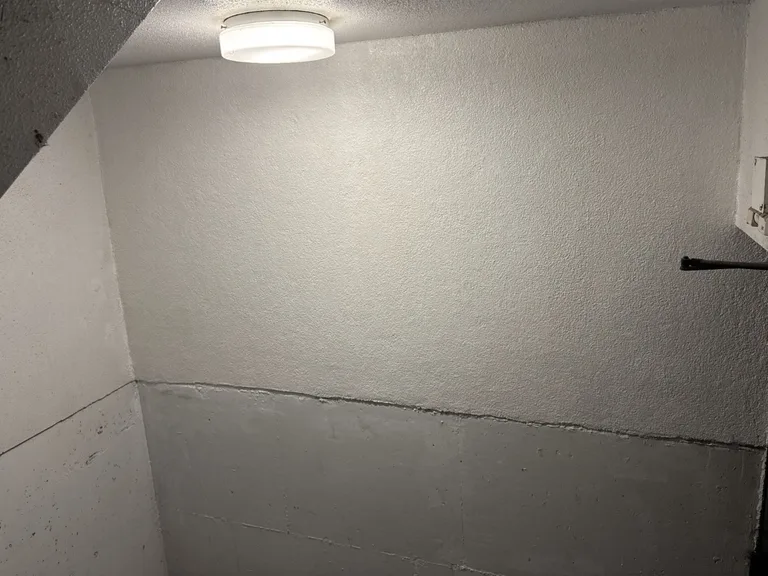 Parkade stairwell wall after plaster repair, smooth and evenly finished under a ceiling light in a parkade stairwell in Port Coquitlam, BC by Pacific Coast Contracting. — after