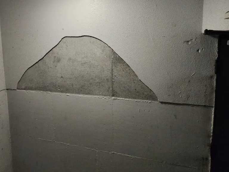 Parkade stairwell wall with a large patch of damaged, exposed plaster before repair in a parkade stairwell in Port Coquitlam, BC by Pacific Coast Contracting. — before