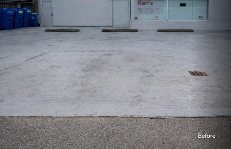 A newly sealed and painted commercial parking lot in front of a building with a "Ken's Dry Cleaning" sign. The concrete is a uniform, fresh grey color with crisp, bright yellow parking lines newly painted. Concrete wheel stops are positioned at the head of each space. The word "After" is overlaid in the bottom right corner. — before